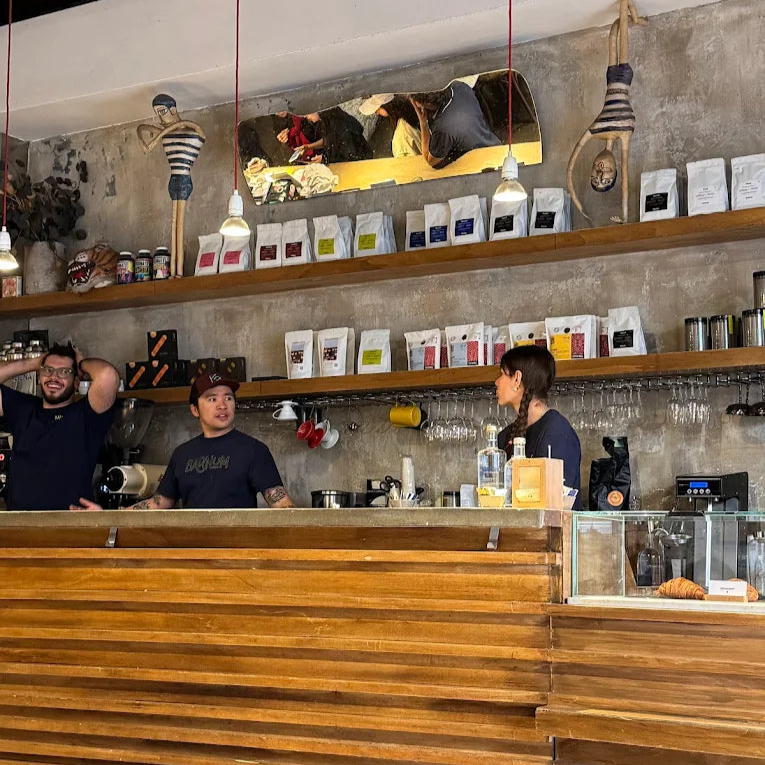 People at a specialty coffee shop called Barnum Coffee in Rome, Italy. A counter with shelves displaying various items in a casual setting