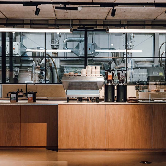 Modern specialty coffee shop interior with wooden counter and with specialty coffee roastery behind glass wall.