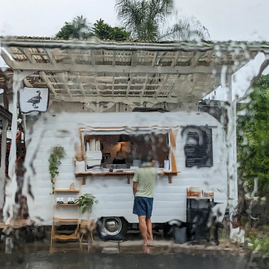 Person standing outside a specialty coffee truck in Hawaii, surrounded by greenery.