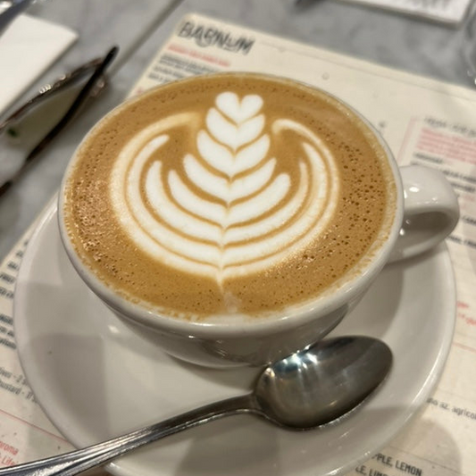 Cappuccino with latte art on a saucer with a spoon, on a table with a newspaper at a third wave coffee shop called Barnum Coffee in Rome, Italy.