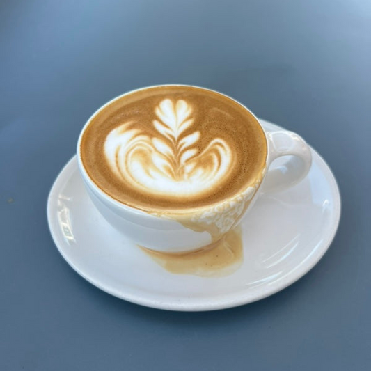 Third wave coffee cappuccino with latte art on a white saucer against a blue background