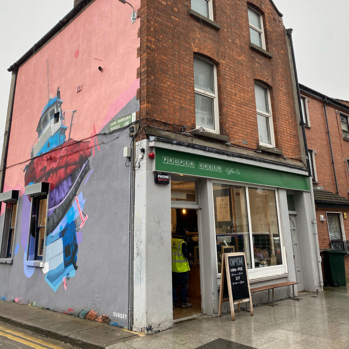 Brick building with a colorful mural on the corner, featuring a store entrance.