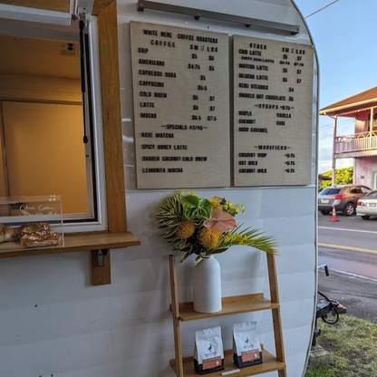 Third wave coffee truck with menu board, flowers, and coffee bags on a wooden shelf in Kona Hawaii.
